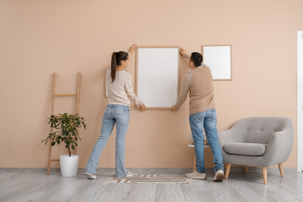 A picture being hung on a wall by a young couple.