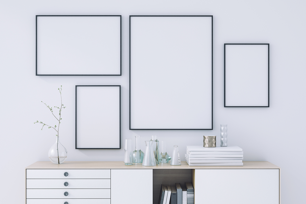 Multiple picture frames on a white wall above a cupboard.