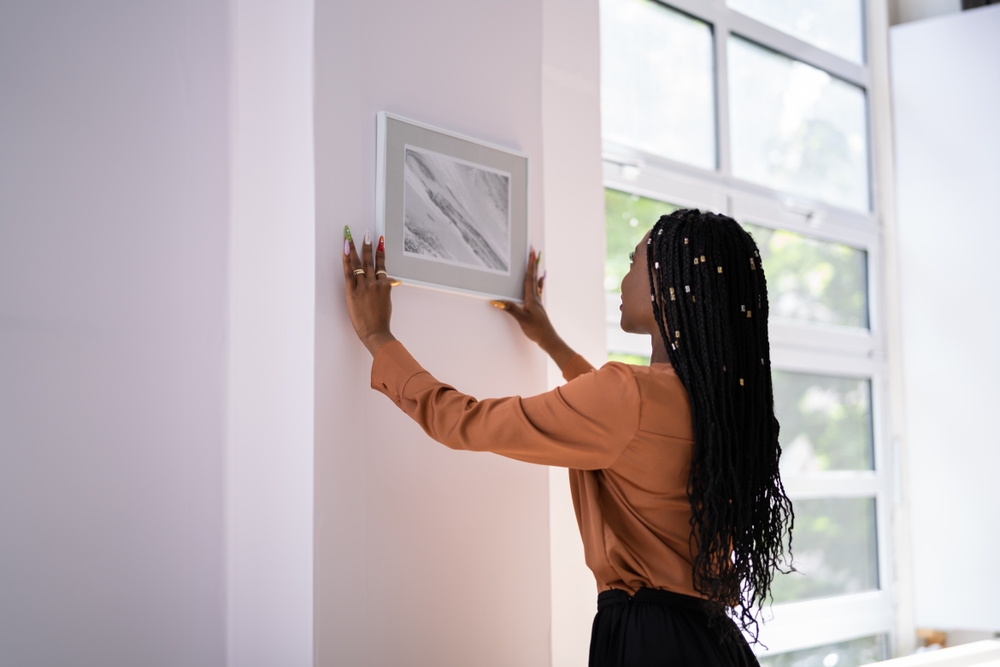 Young,Woman,Putting,Photo,Frame,On,White,Wall